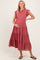 woman wearing a rust-colored maternity dress with ruffle sleeves and a tiered skirt, gently cradling her baby bump