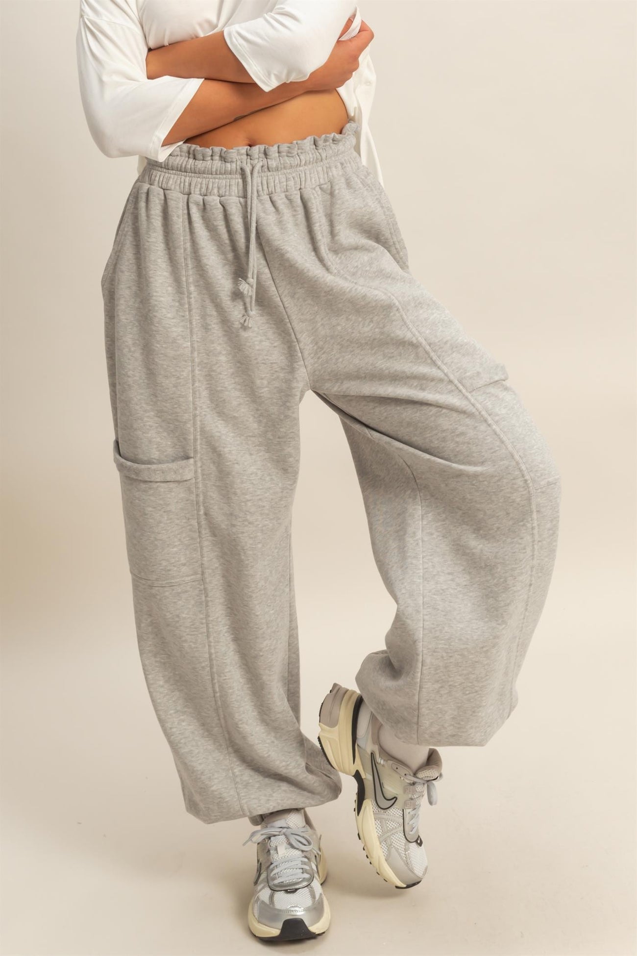 woman wearing gray relaxed fit sweatpants with a drawstring waist and side pocket, styled with sneakers