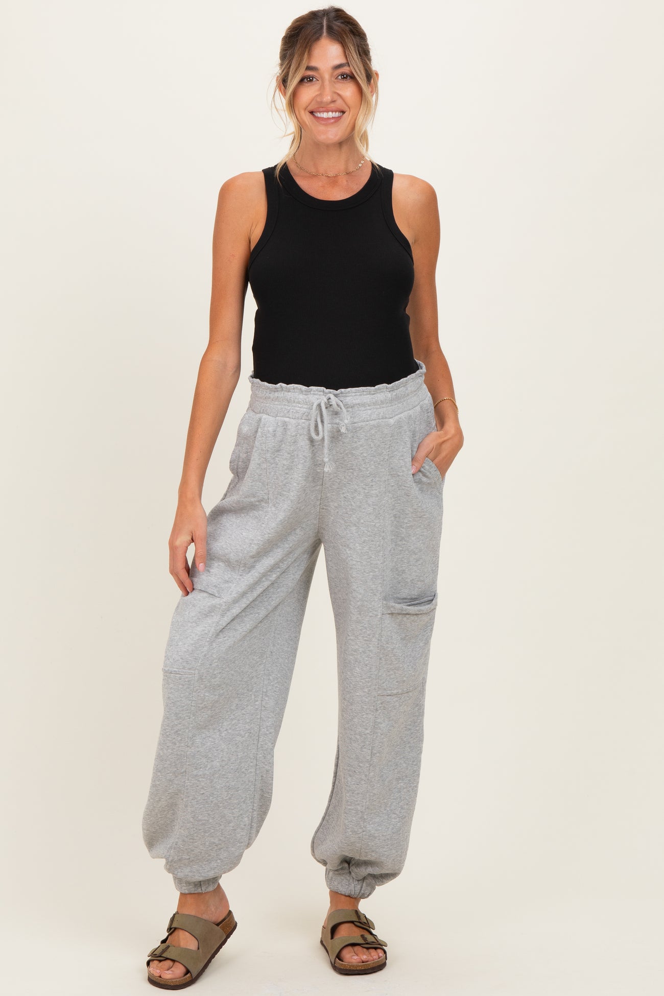 woman wearing a black tank top and gray maternity jogger pants with pockets, standing and smiling