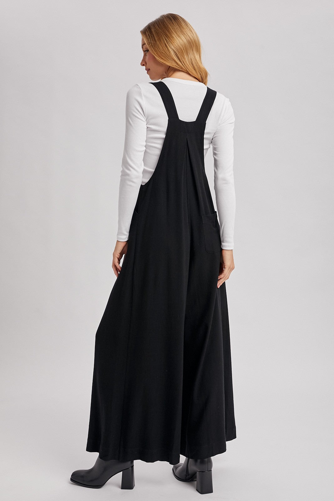 woman wearing a black maxi dress with adjustable straps and a relaxed fit, facing away from the camera