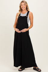woman wearing a black maternity dungaree dress over a gray top and holding her baby bump
