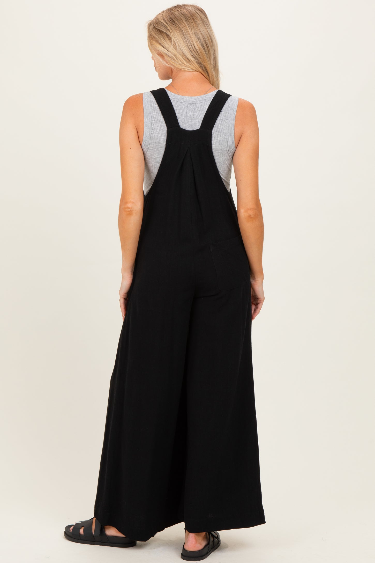 woman wearing a black maternity overall jumpsuit with wide legs, seen from the back