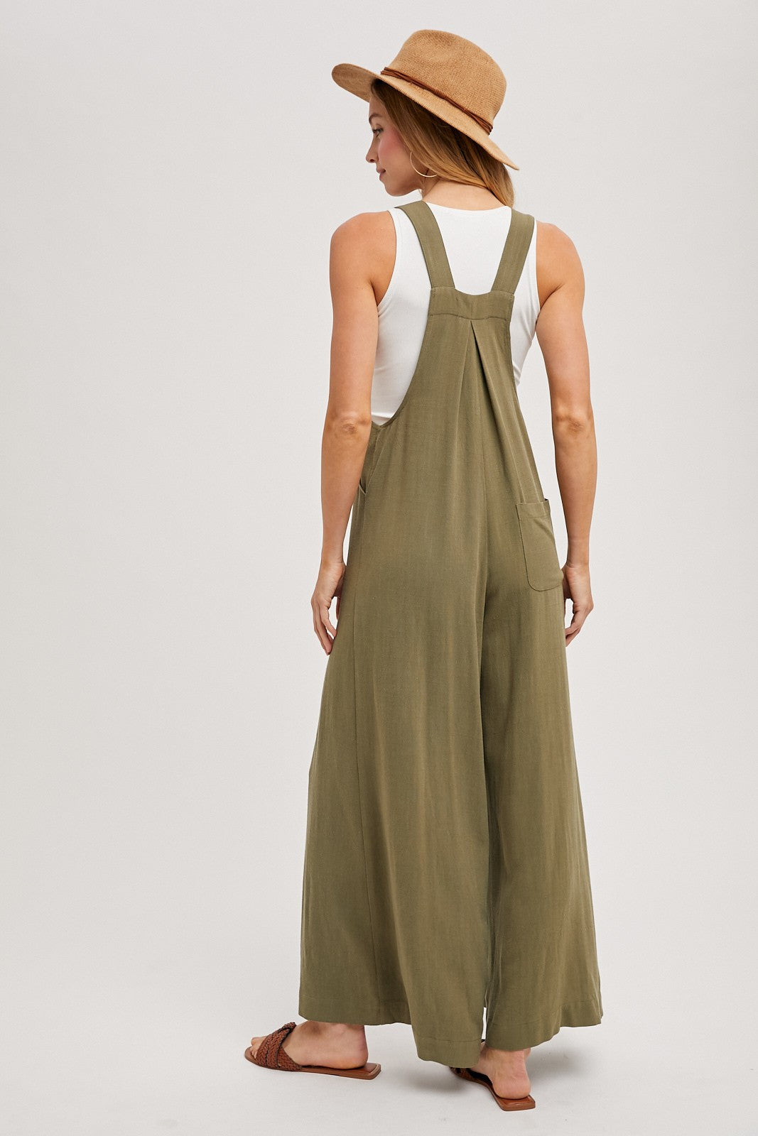 woman wearing a green long wide-leg jumpsuit and a tan hat, viewed from the back