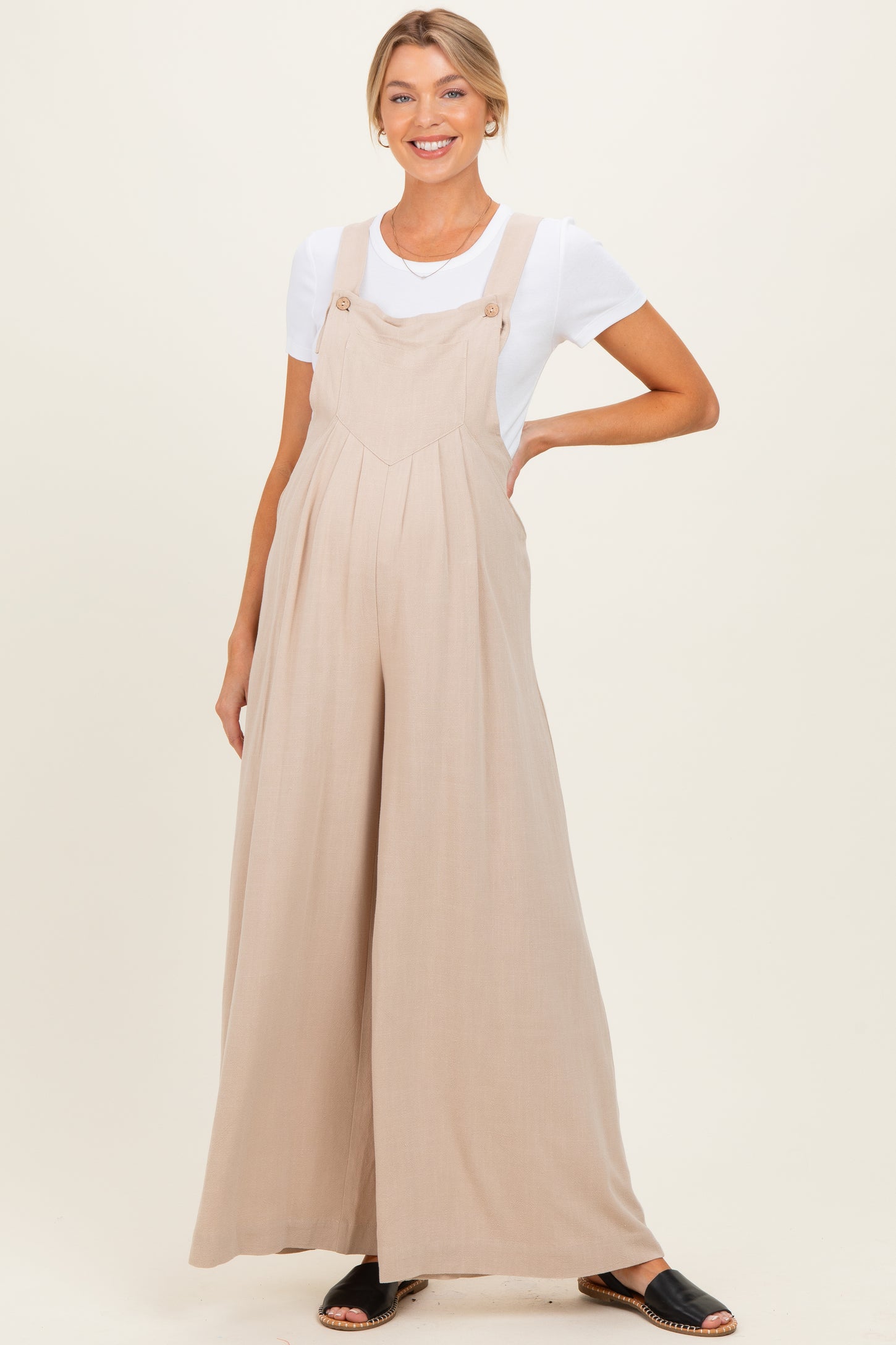 woman wearing a light beige maternity jumpsuit with adjustable straps and a flowy wide-leg style