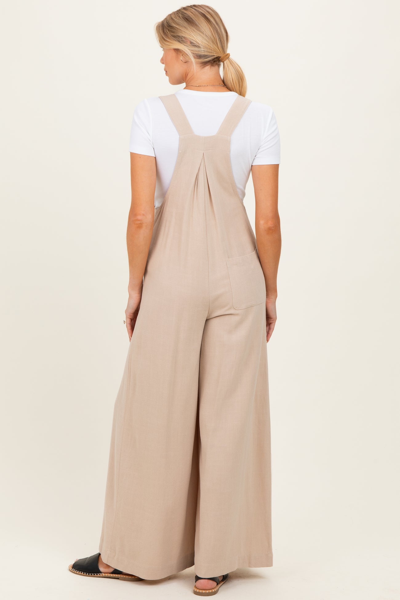 woman wearing beige maternity overalls with wide legs, shown from the back