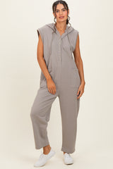 woman wearing a gray sleeveless jumpsuit with a hood and button details, standing against a neutral background