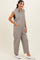 woman wearing a gray sleeveless hooded jumpsuit with button details and side pockets