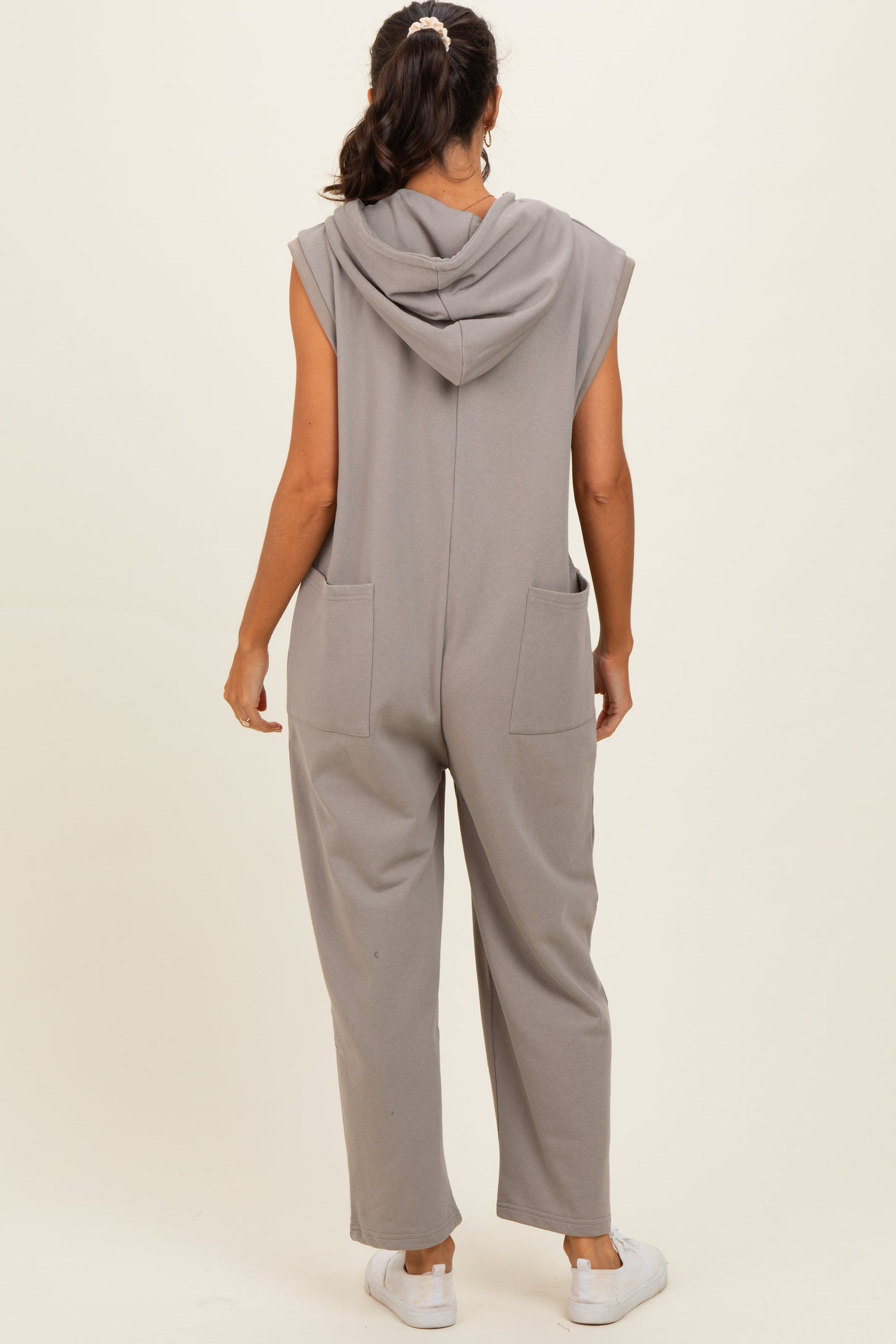 woman wearing a sleeveless gray hooded jumpsuit with side pockets, seen from the back