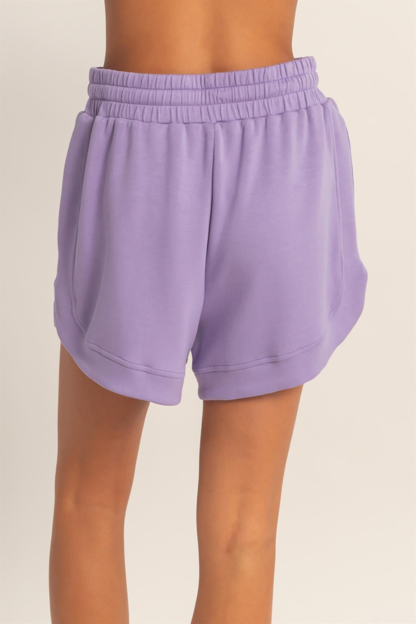 women wearing purple lightweight athletic shorts with an elastic waistband and side pockets, seen from the back