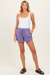 woman wearing a white tank top and lavender maternity shorts with pockets, standing fashionably
