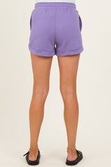 woman wearing lavender maternity shorts with a relaxed fit and side pockets, standing with her back to the camera