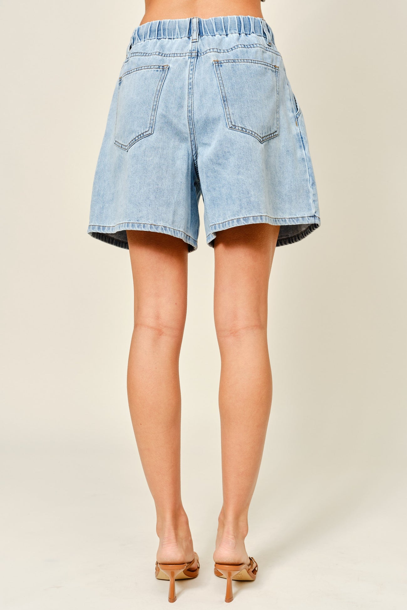 woman wearing light blue high-waisted denim shorts with an elastic waistband, shown from the back