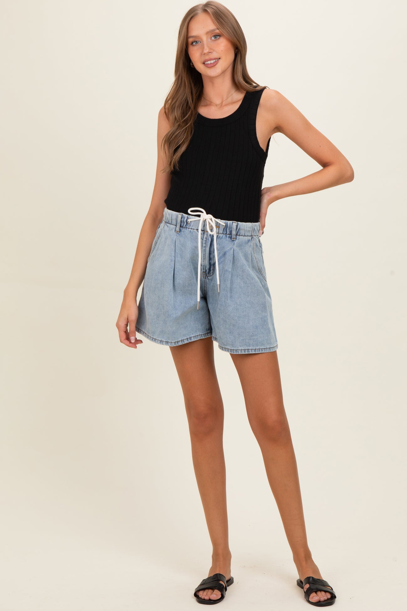 woman wearing a black ribbed tank top and denim maternity shorts with a drawstring waist