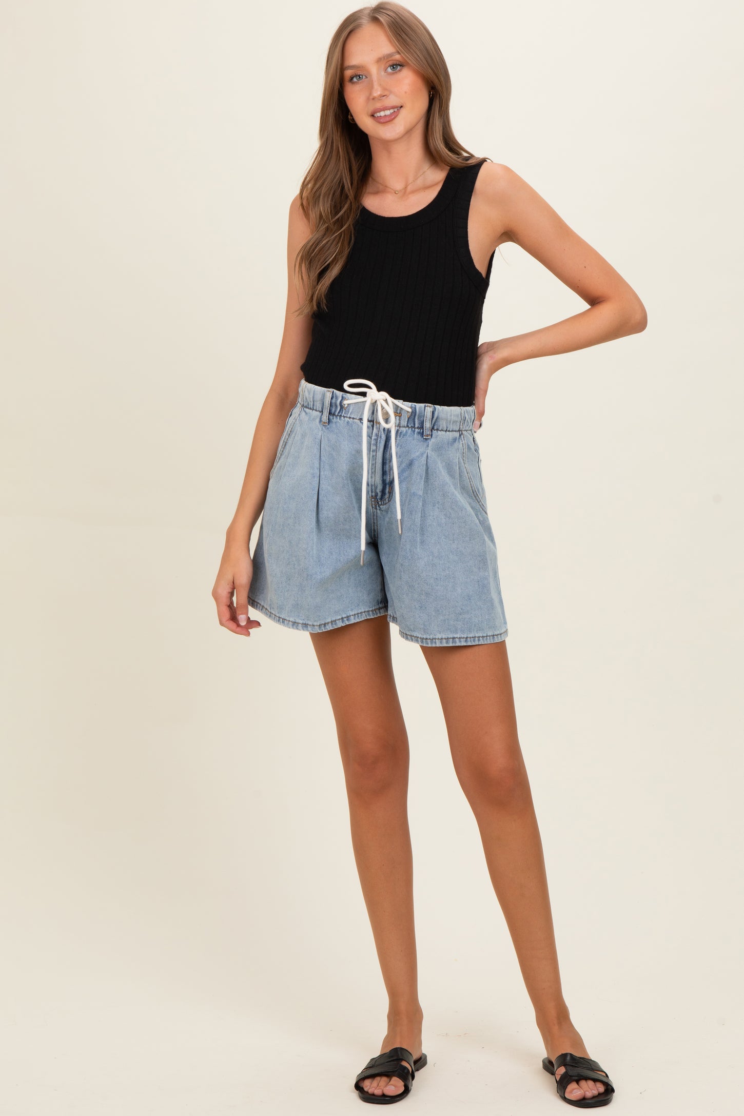 woman wearing a black ribbed tank top and denim maternity shorts with a drawstring waist