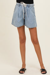 maternity wear light blue denim shorts with a drawstring waist and pleated front, model standing with one leg forward