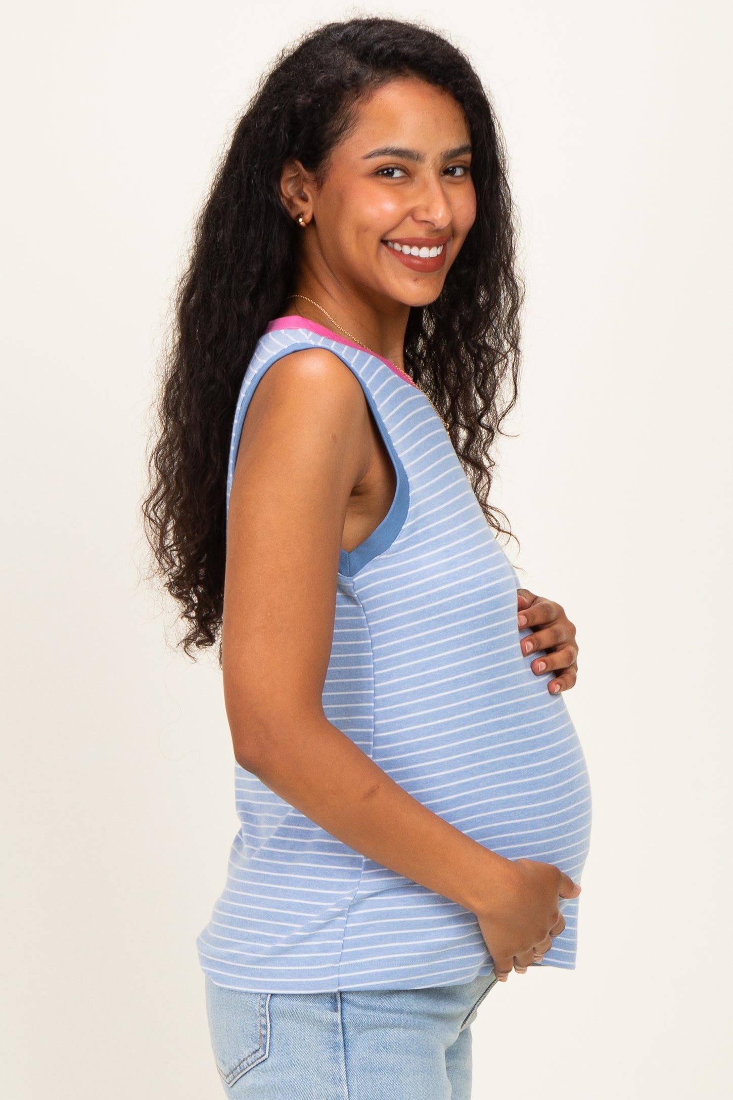 woman wearing a light blue strip maternity tank top, smiling and holding her baby bump