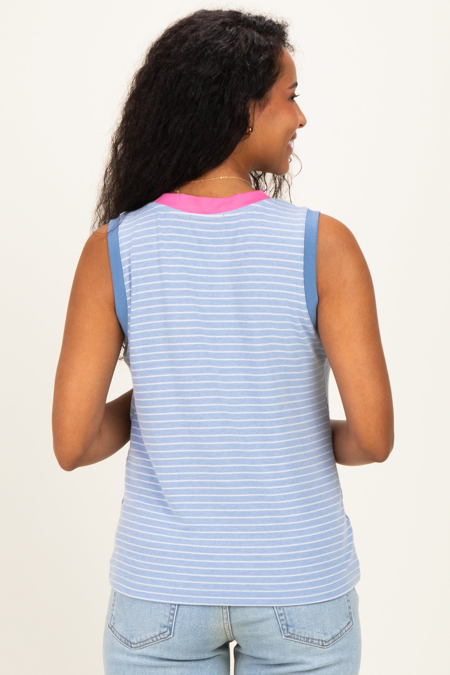 woman wearing a striped blue maternity tank top with a pink neckline, showing her back and styled with light blue jeans