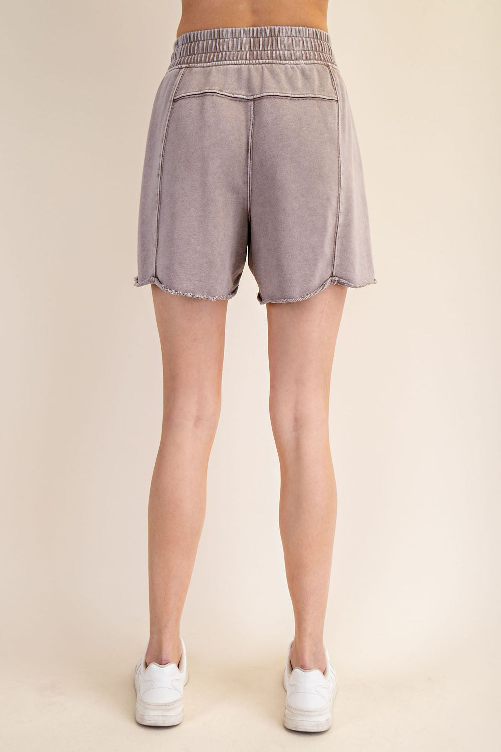 woman wearing light grey casual shorts with a frayed hem and elastic waistband, viewed from the back