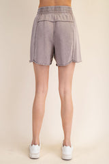 woman wearing light grey casual shorts with a frayed hem and elastic waistband, viewed from the back