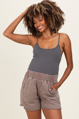 woman wearing a gray maternity tank top and brown maternity shorts, smiling and posing with one hand in her hair