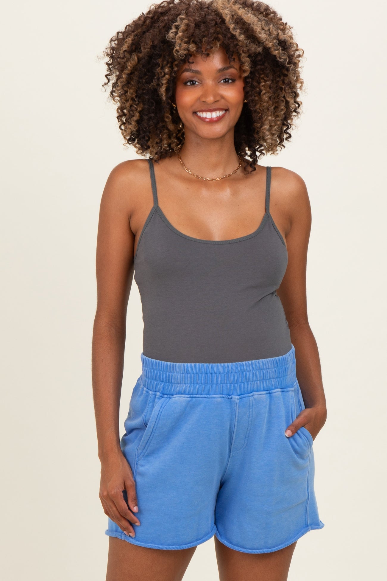 woman wearing a gray maternity tank top and blue maternity shorts with pockets, smiling at the camera