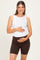 woman wearing a white ribbed maternity tank top and brown maternity bike shorts, holding her baby bump