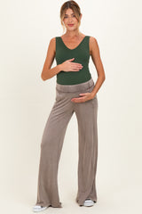 woman wearing a green sleeveless maternity top and beige wide-leg maternity pants, holding her baby bump
