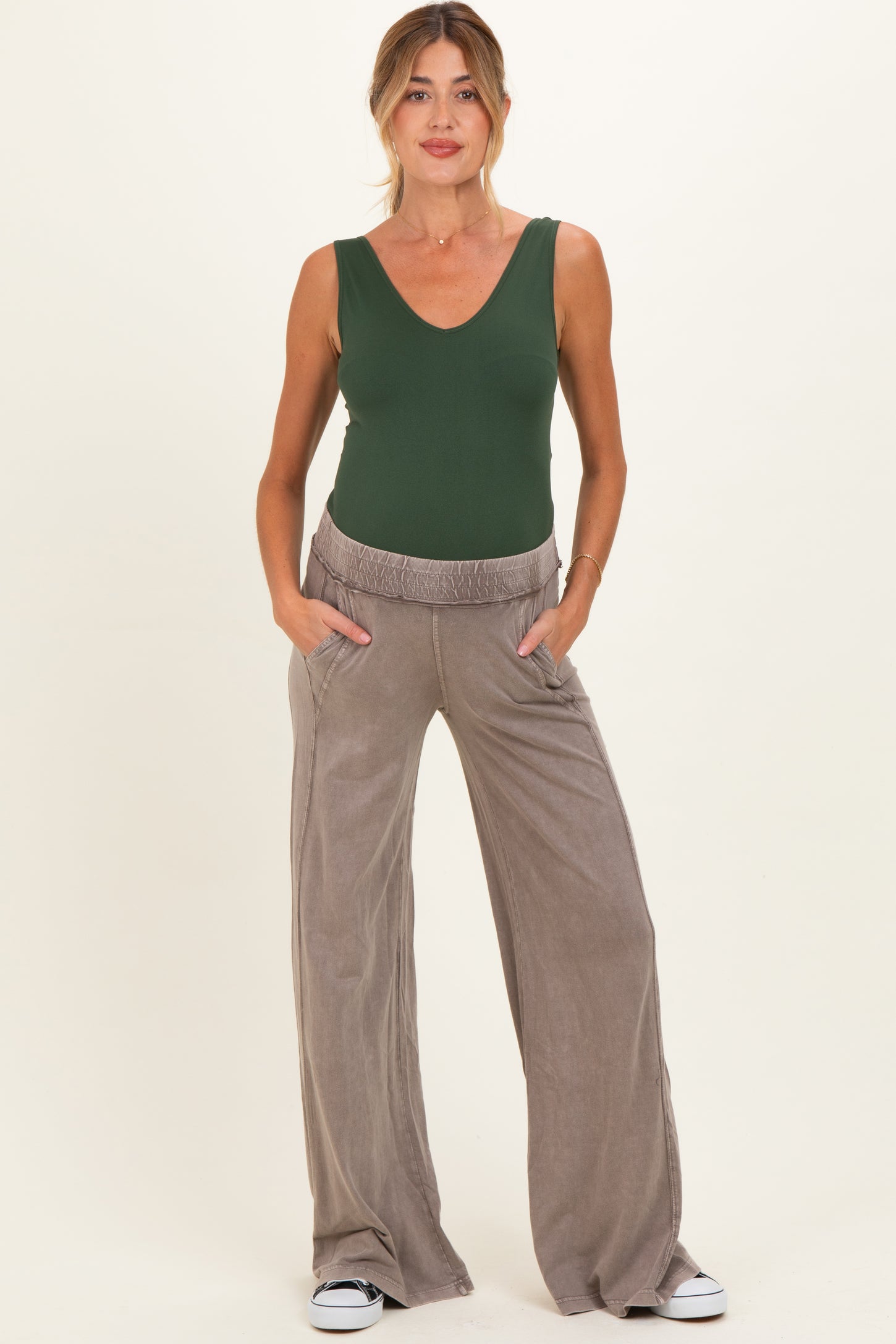 woman wearing a green maternity bodysuit and taupe wide-leg maternity pants with pockets
