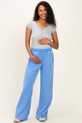 woman wearing a gray short sleeve henley top and blue maternity pants, gently holding her baby bump