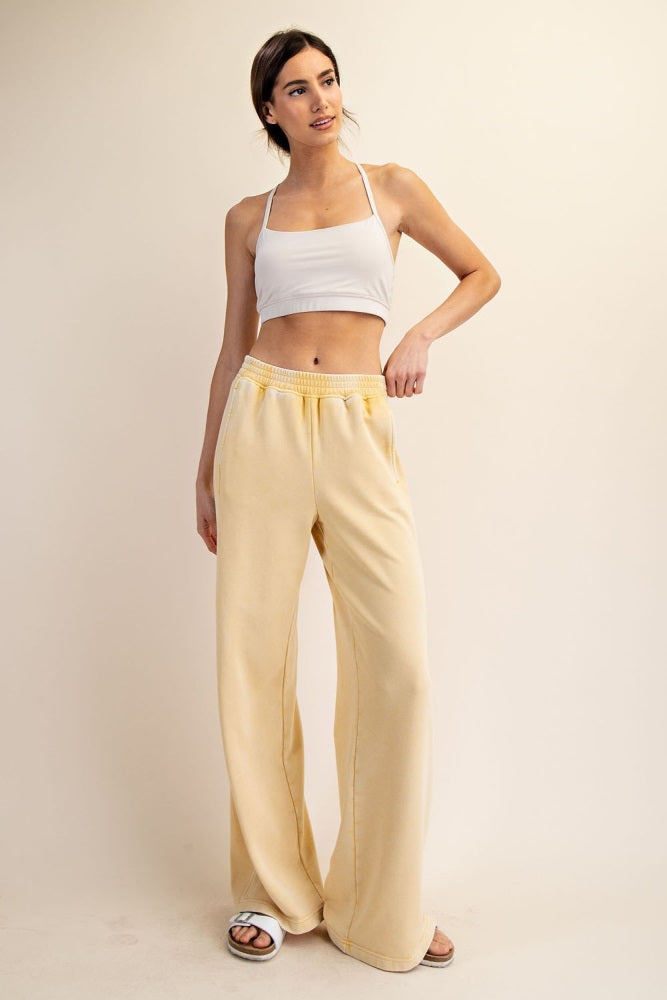 woman wearing a white cropped top and light yellow wide-leg pants, standing with one hand on her hip