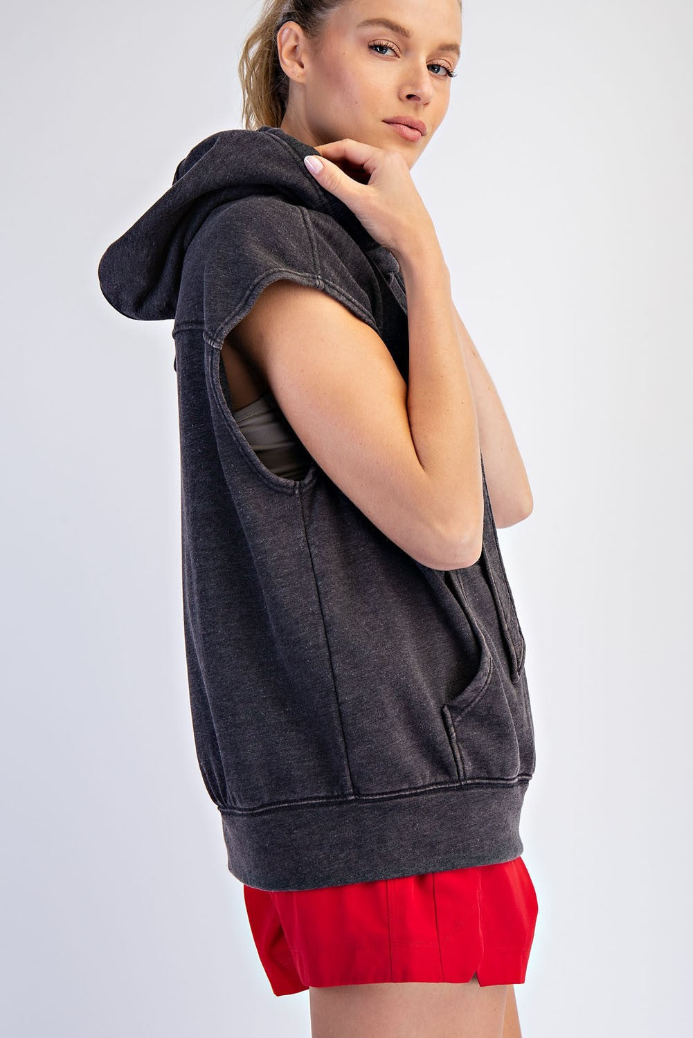 woman wearing a charcoal sleeveless hoodie with a front pocket and red athletic shorts
