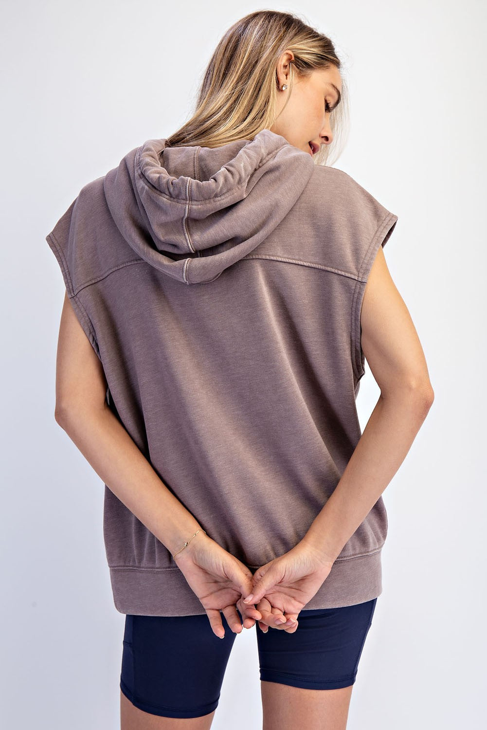 woman wearing a brown sleeveless hoodie from the back with a relaxed fit and hooded design