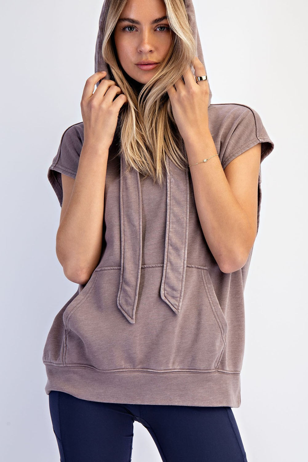 woman wearing a taupe sleeveless hoodie with a front pocket and drawstring detail