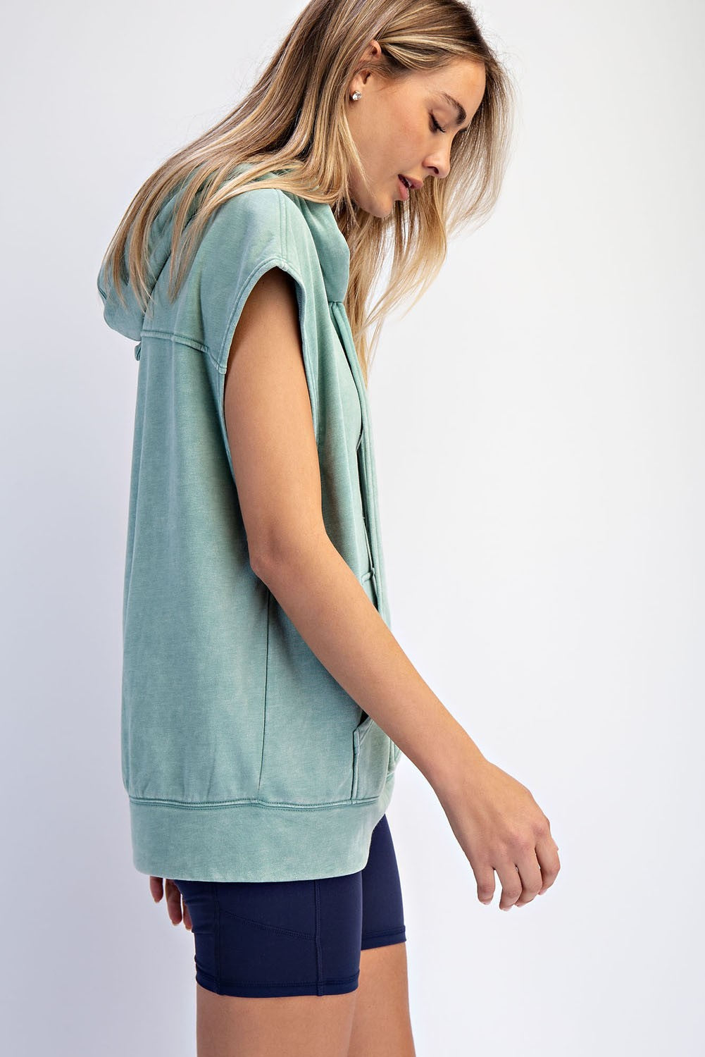 woman wearing a mint green sleeveless hoodie with a hood, styled with navy bike shorts