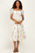 woman wearing a white floral midi dress with puff sleeves and a smocked bodice, standing with hands at her sides