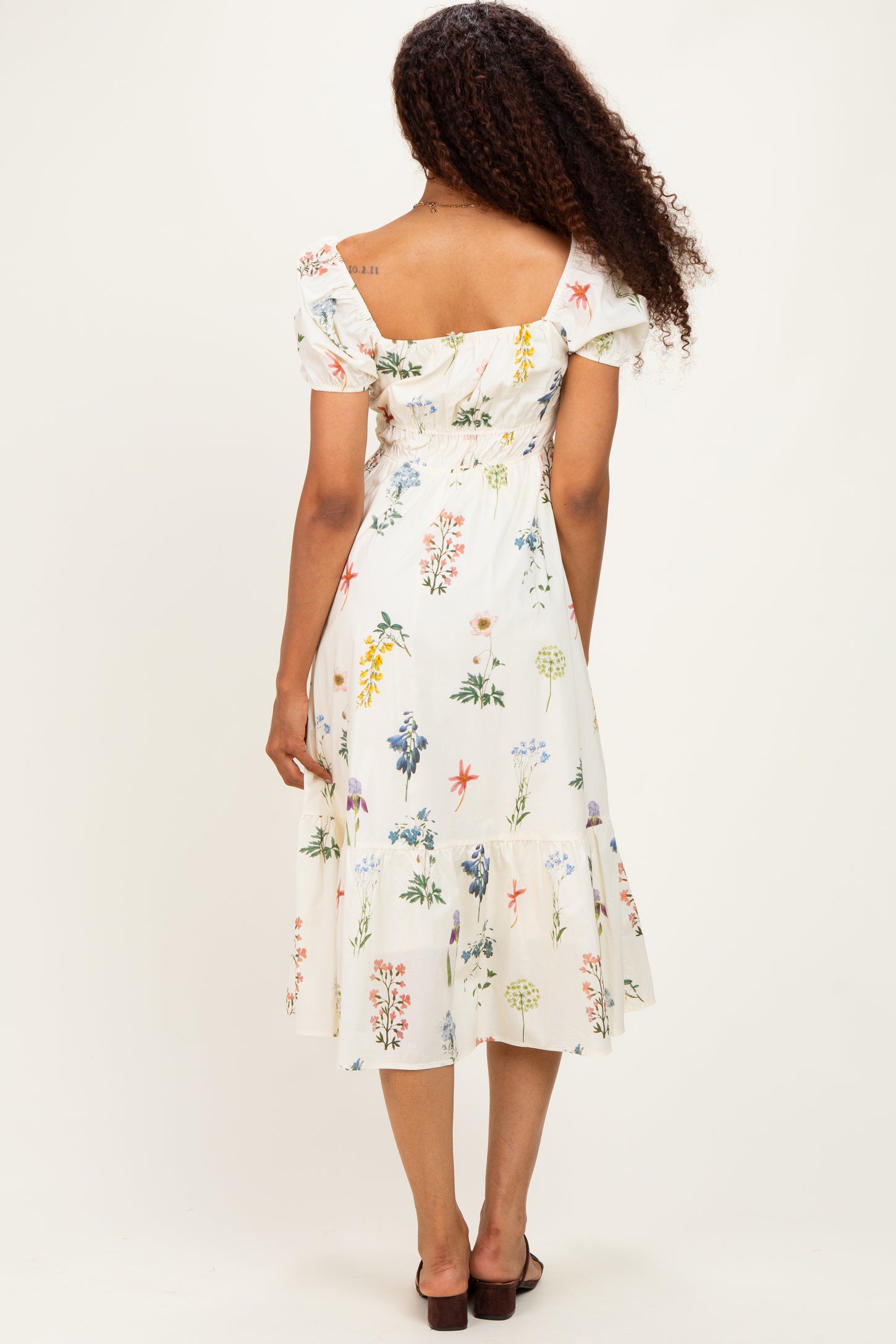 woman wearing a floral print off-the-shoulder midi dress with a ruffled hem and fitted bodice, seen from the back