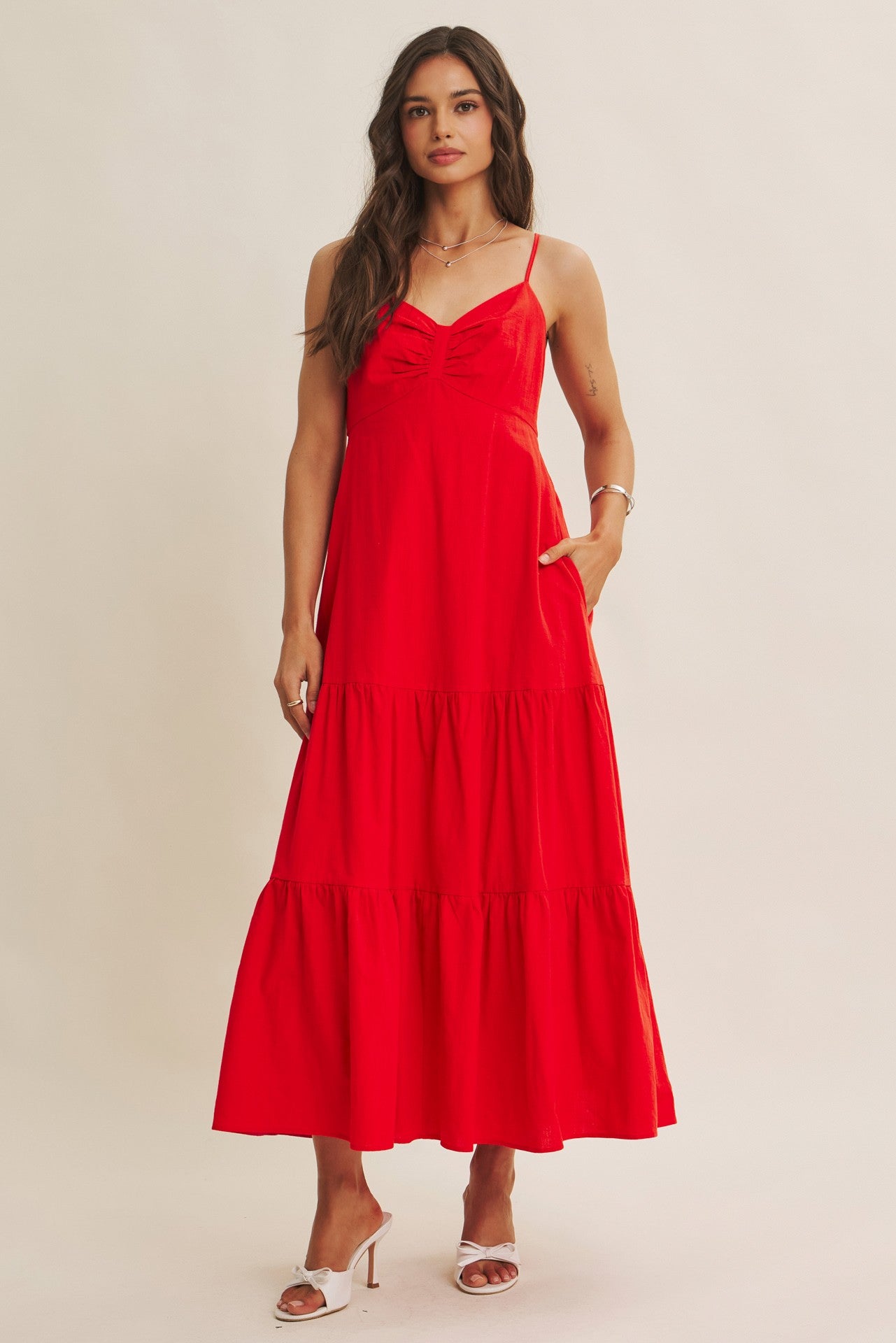 woman wearing a vibrant red maxi dress with adjustable straps and tiered skirt, featuring pockets and a fitted bodice