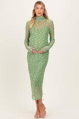 woman wearing a green sheer maternity dress with white polka dots and long sleeves, gently cradling her baby bump