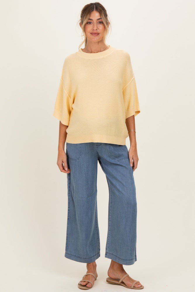 woman wearing a light yellow oversized maternity sweater and wide-leg jeans, with a visible baby bump