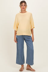 woman wearing a light yellow oversized maternity sweater and wide-leg jeans, with a visible baby bump