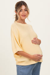 woman wearing a yellow oversized maternity sweater and holding her baby bump