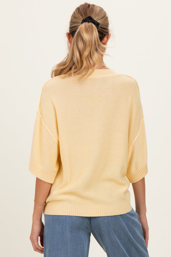 woman wearing a yellow oversized maternity sweater, view of the back, styled with blue denim pants