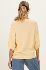 woman wearing a yellow oversized maternity sweater, view of the back, styled with blue denim pants