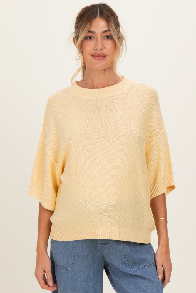 woman wearing a light yellow oversized maternity knit sweater with short sleeves and a relaxed fit