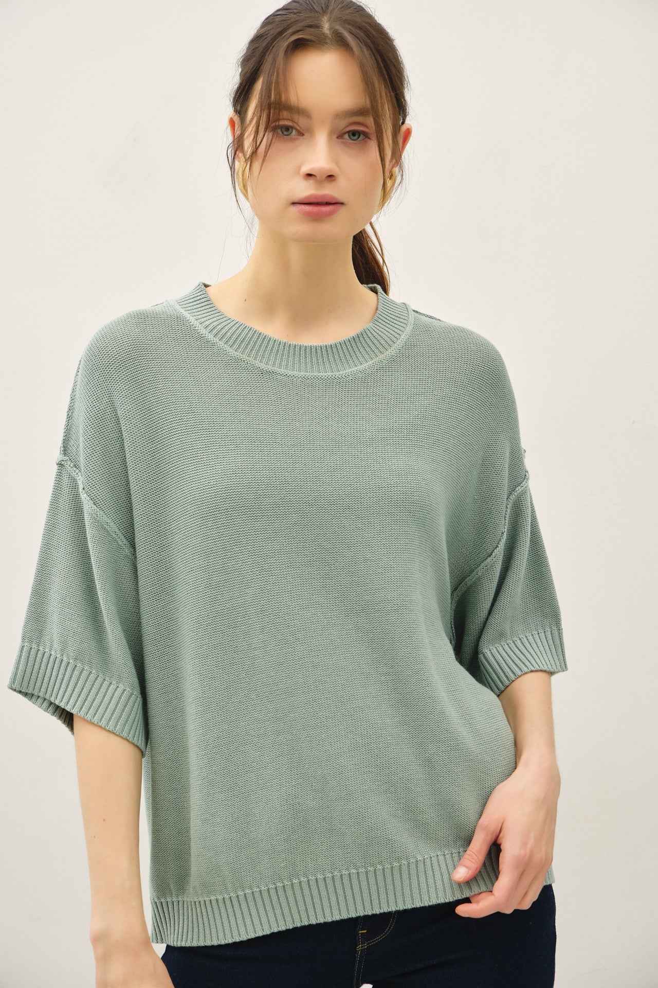 woman wearing a loose-fitting, light green short-sleeve sweater with a round neckline and ribbed detailing