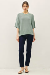 woman wearing a light green oversized knit sweater and dark blue jeans, standing on a plain background