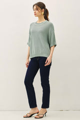 woman wearing a light green oversized sweater and dark blue skinny jeans, standing sideways with a casual pose