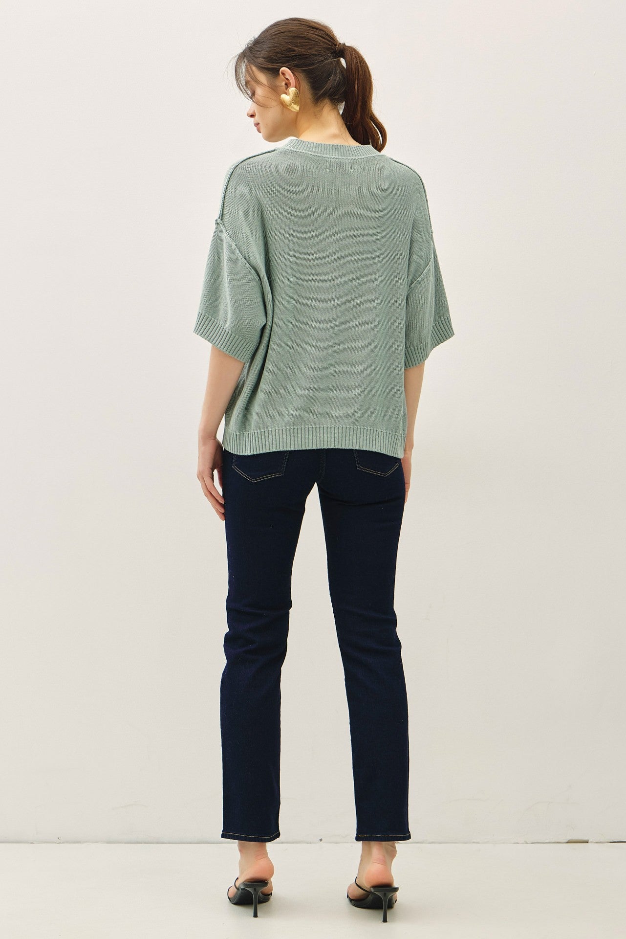 woman wearing a loose-fitting sage green sweater paired with dark skinny jeans, viewed from the back