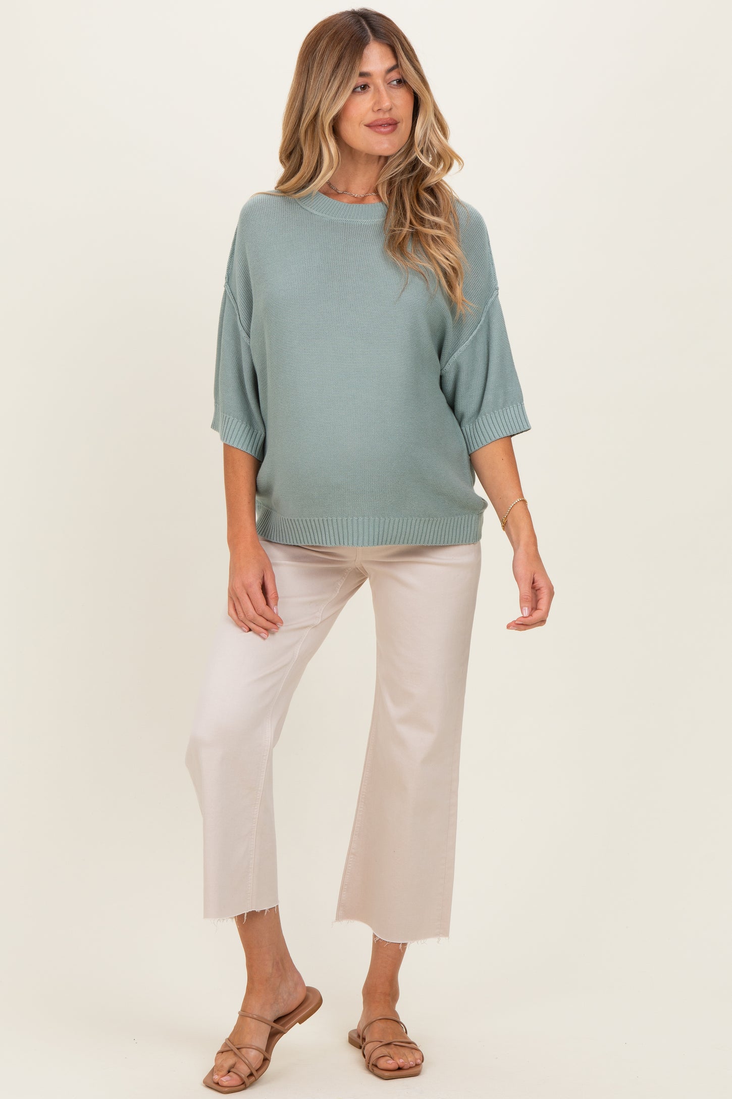 woman wearing a light green oversized knit maternity sweater and cream wide-leg pants, showing her baby bump