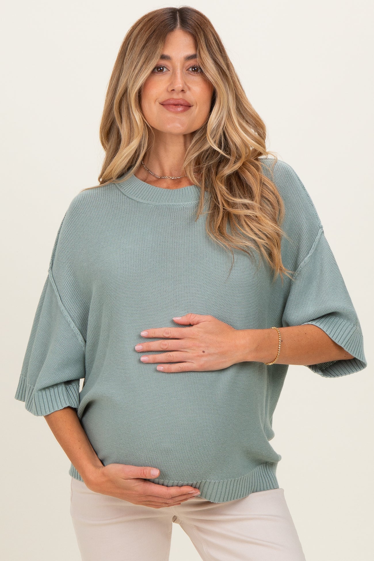 woman wearing a light green maternity sweater and holding her baby bump